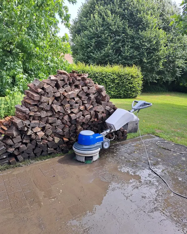 Borstelmachine van Clean Floors op een nat terras naast een houtstapel