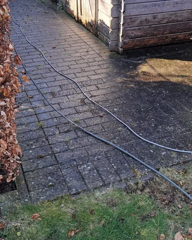 Donker, nat klinkerpad naast een tuinhuis met waterslang